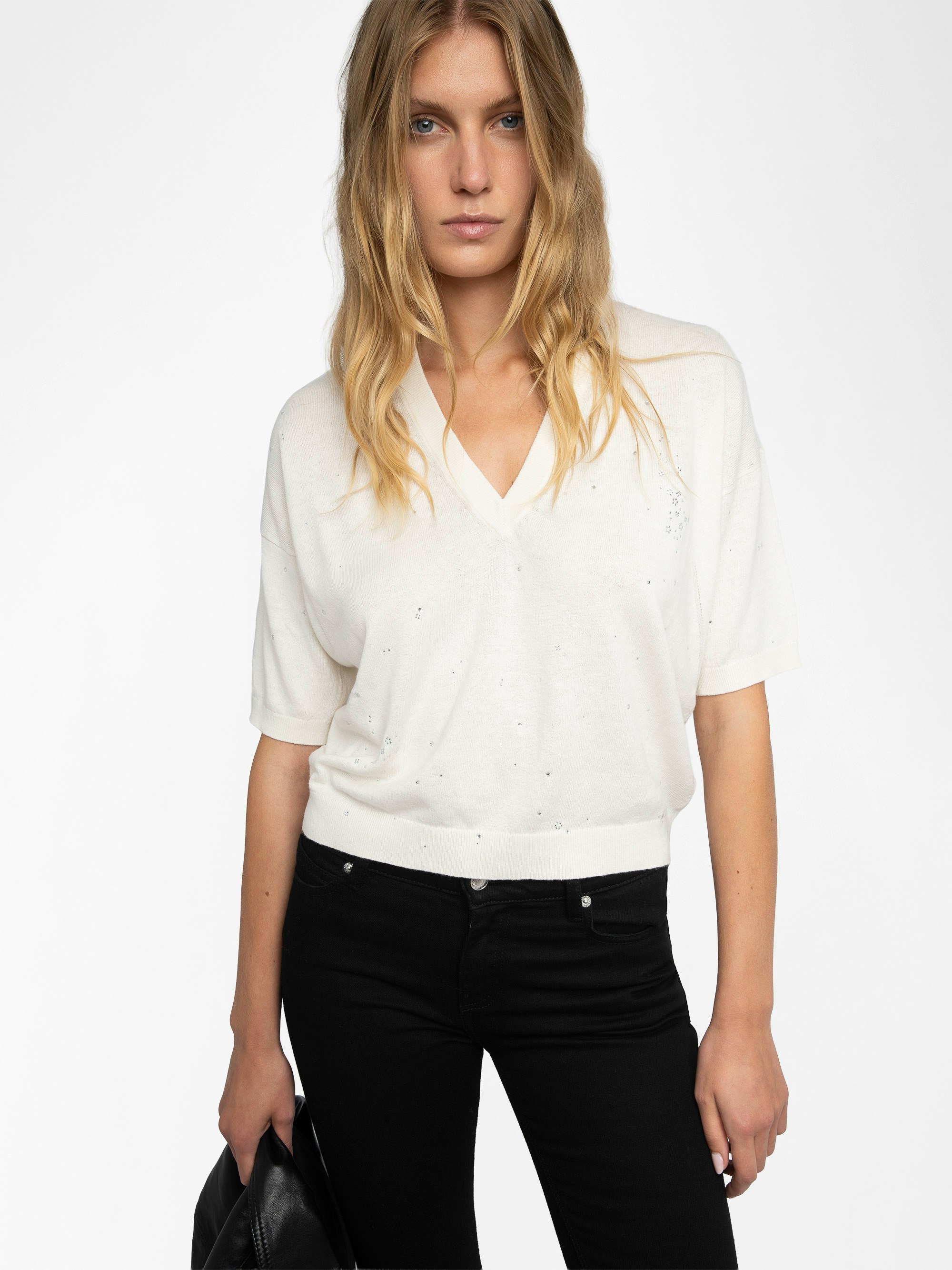 Wully Diamanté Sweater - Cozy meets cool with a touch of sparkle. This ultra-soft white rhinestone sweater wraps you in effortless warmth without losing its edge. Shimmering crystal accents trace the neckline and scatter across the front, delivering refined, rock-chic glamour. A clean V neck and short sleeves let the white rhinestone sweater layer under leather or stand alone over denim, carrying laid-back polish from crisp mornings to late-night sets.