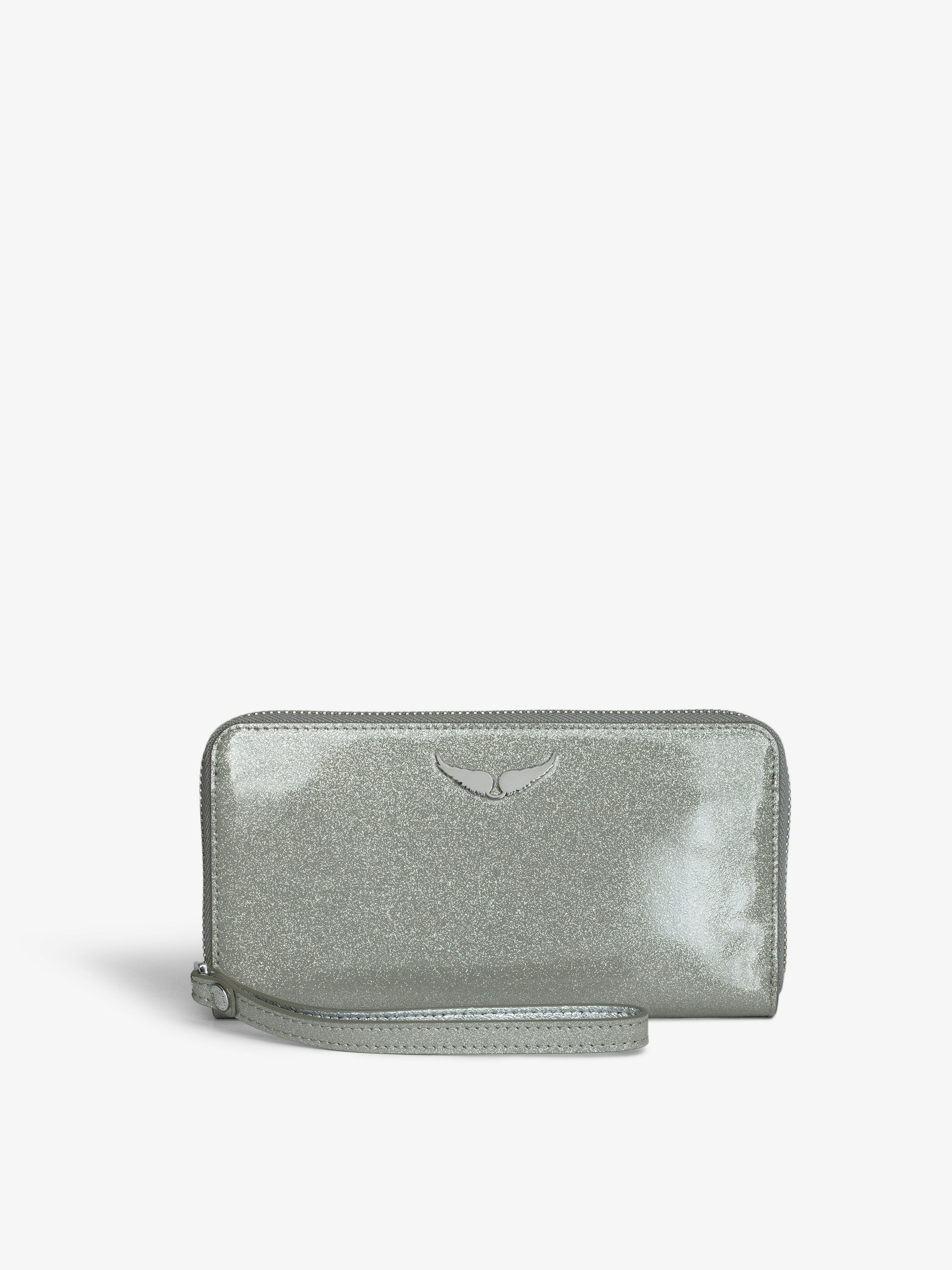 Brieftasche Compagnon Infinity Patent - Brieftasche aus silbernem Lackleder mit Pailletten, Verschlussriemen und einem Flügel-Charm.