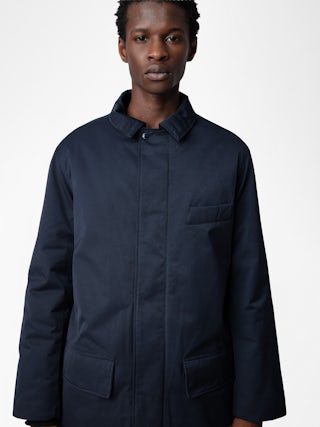 Mel Coat - Unisex mid-length coat featuring a rubber studio badge.